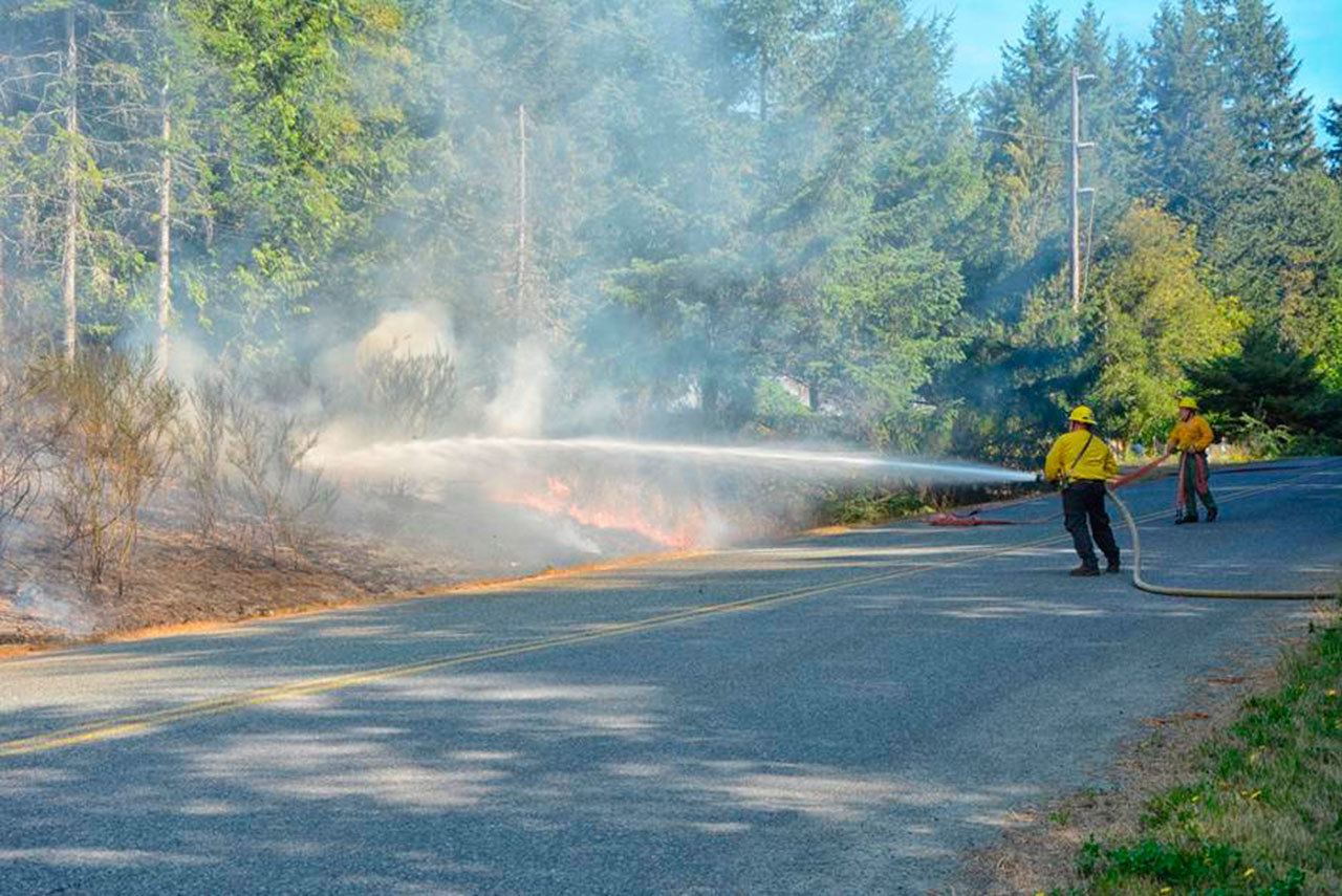Clallam County Fire District No. 2 firefighters hose down the brush fire Tuesday. (Jay Cline/Clallam County Fire District No. 2)