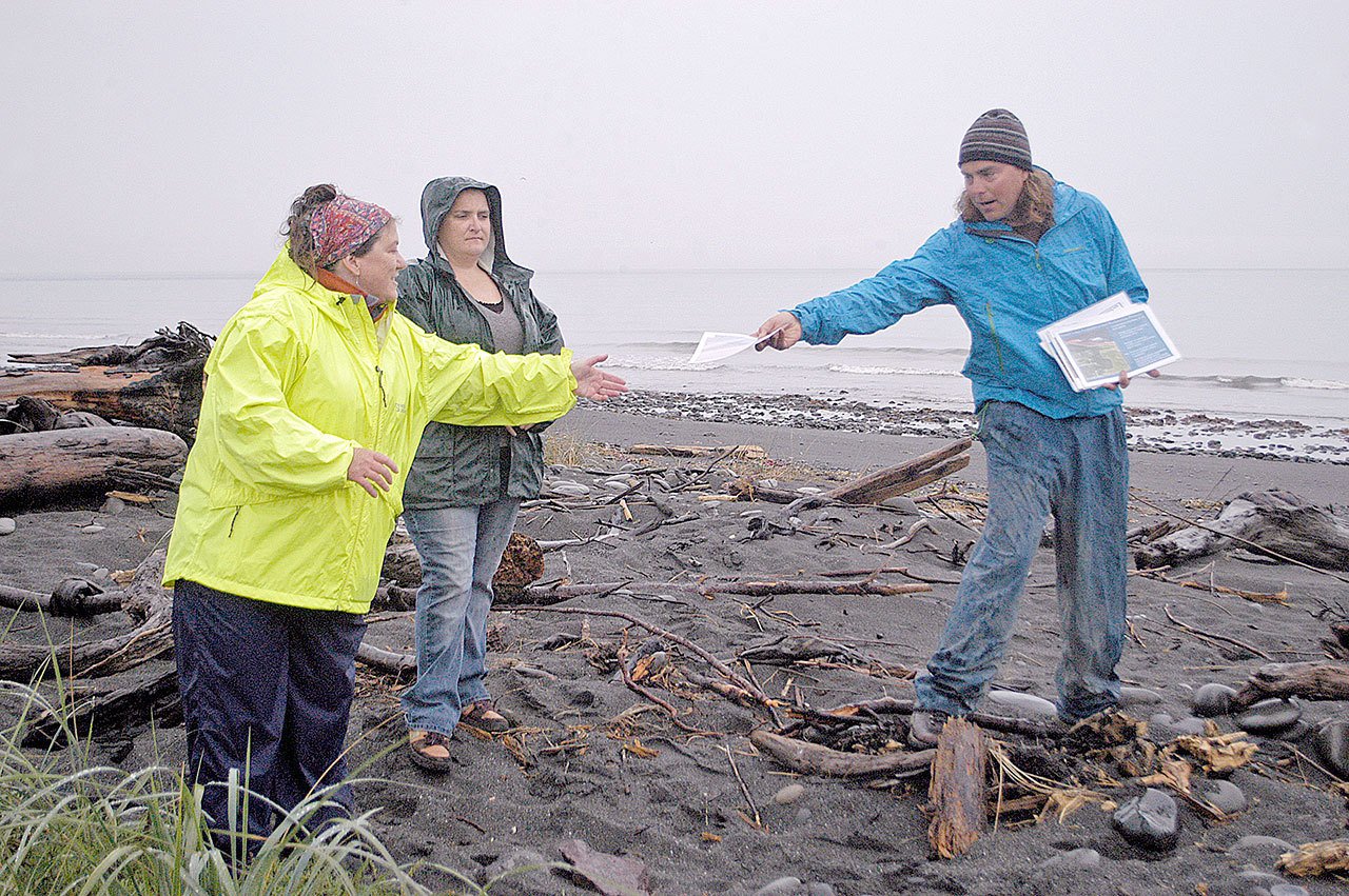 Jamie Michel, Coastal Watershed Institute nearshore biologist, right, hands a pamphlet on beach restoration to CWI Executive Director Anne Shaffer while addressing visitors who turned out to catch a glimpse of the renewed Beach Lake shoreline, located just east of the Elwha River estuary. At middle is Tara McBride, CWI nearshore biologist. (Chris McDaniel/Peninsula Daily News)