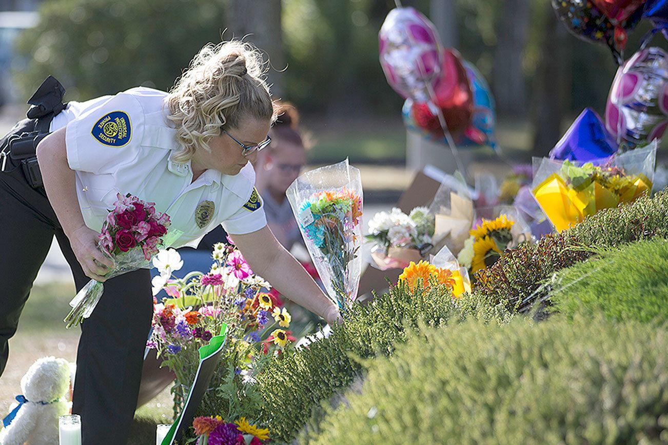 A security guard working at the Cascade Mall places flowers at a makeshift memorial Sunday in Burlington to the five victims killed in a shooting at the mall Friday. The 20-year-old man suspected of killing the five people with a rifle at a Macy’s makeup counter had a string of run-ins with the law in recent years, including charges he assaulted his stepfather. (Stephen Brashear/The Associated Press)