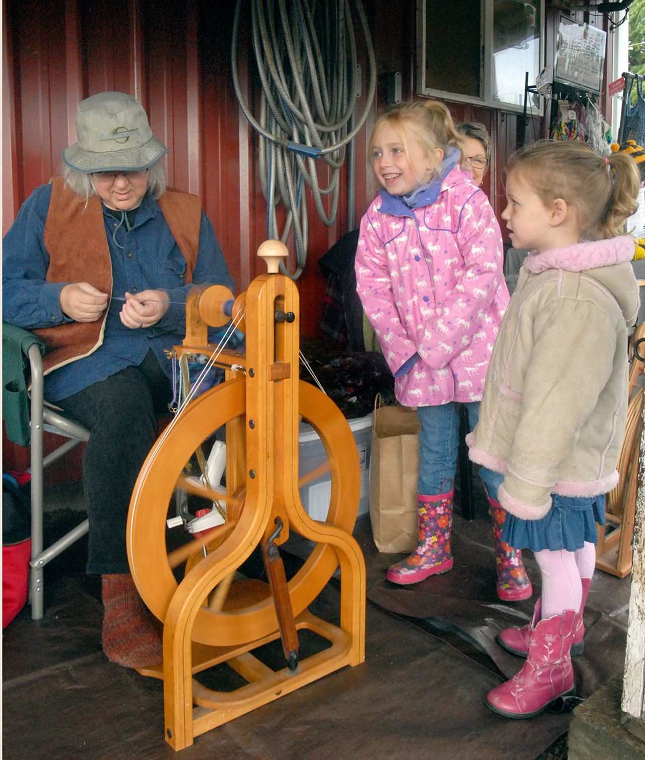 Alexia Fuller, 5, center, and Adeline Slezak, 3, both of Sequim, watch as Alison Sell, a member of the North Olympic Shuttle and Spindle Guild, spins wool into fiber at Lurkalee Gaare sheep farm near Agnew, one of seven farms and businesses taking part at the 20th annual Clallam County Farm Tour on Saturday. The event served as a celebration of agriculture and farmland. (Keith Thorpe/Peninsula Daily News)