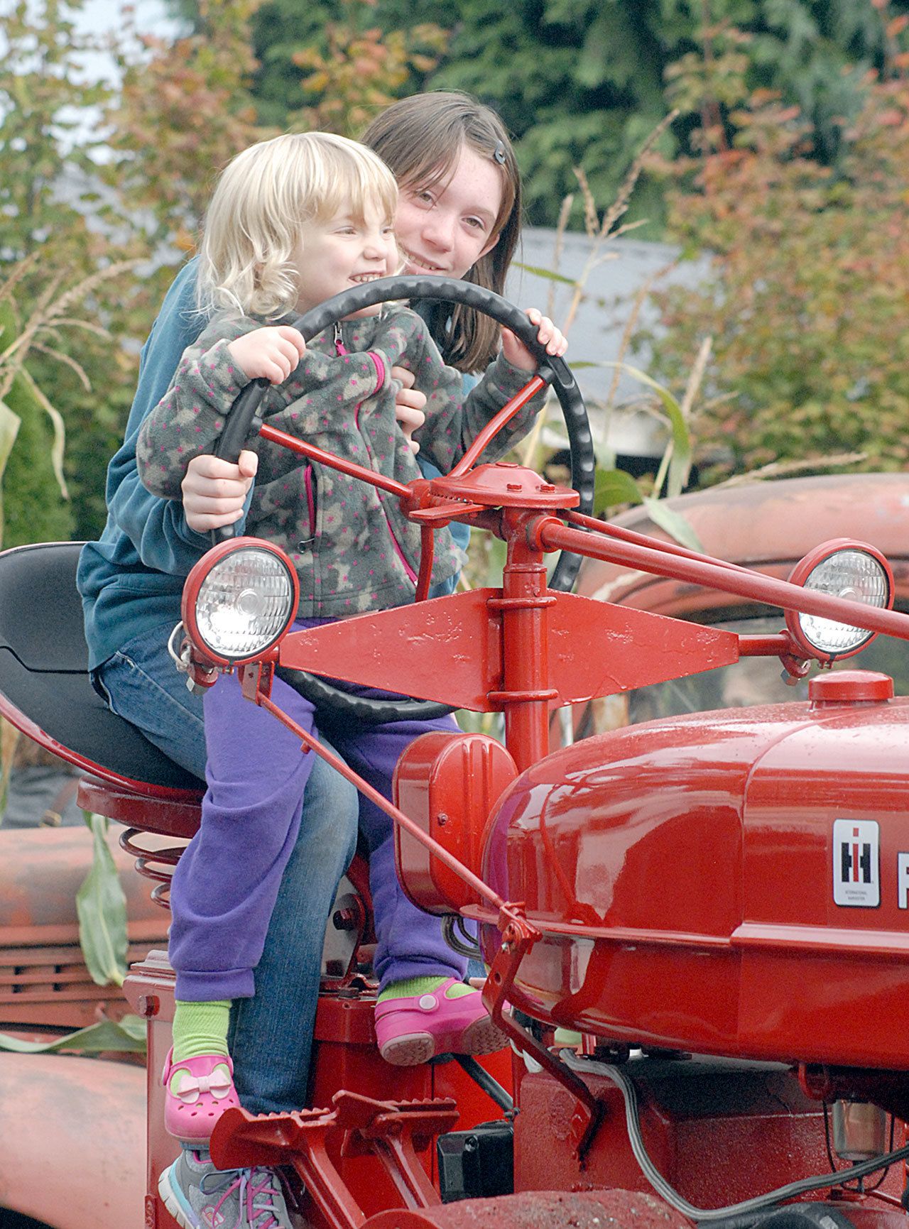 Madisyn Heistand, 10, and Abigaile Heistand, 3, both of Port Angeles, sit at the controls of an antique tractor at Agnew Grocery on Saturday. The grocery was one of seven farms and businesses taking part in the 20th annual Clallam County Farm Tour, a celebration of the agricultural heritage of the Dungeness Valley. (Keith Thorpe/Peninsula Daily News)
