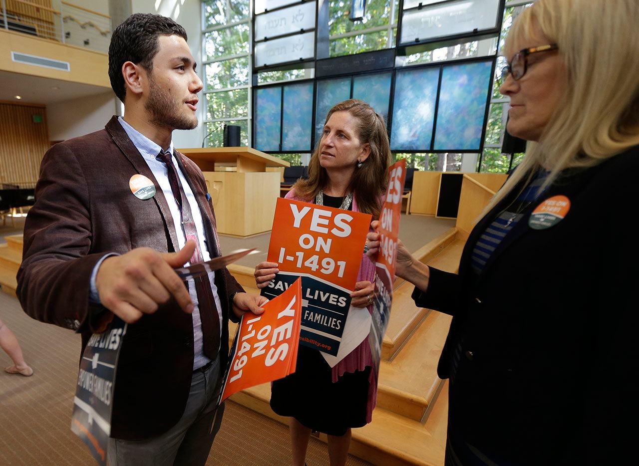 Dujie Tahat, left, hands out posters to Marilyn Balcerak, right, and Rep. Tana Senn, D-Mercer Island, center, before a Sept. 21 news conference in Bellevue promoting Initiative 1491, which will be on the ballot in the November elections. (Ted S. Warren/The Associated Press)