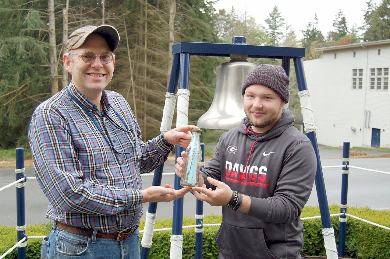 Dave Grant, left, a Navy archaeologist, and Ben Carlson, an archaeological assistant, hold a message in a bottle that was found on Indian Island. It was left off Port Williams Beach by Sequim teens in 2010 and found Oct. 18, six years later.