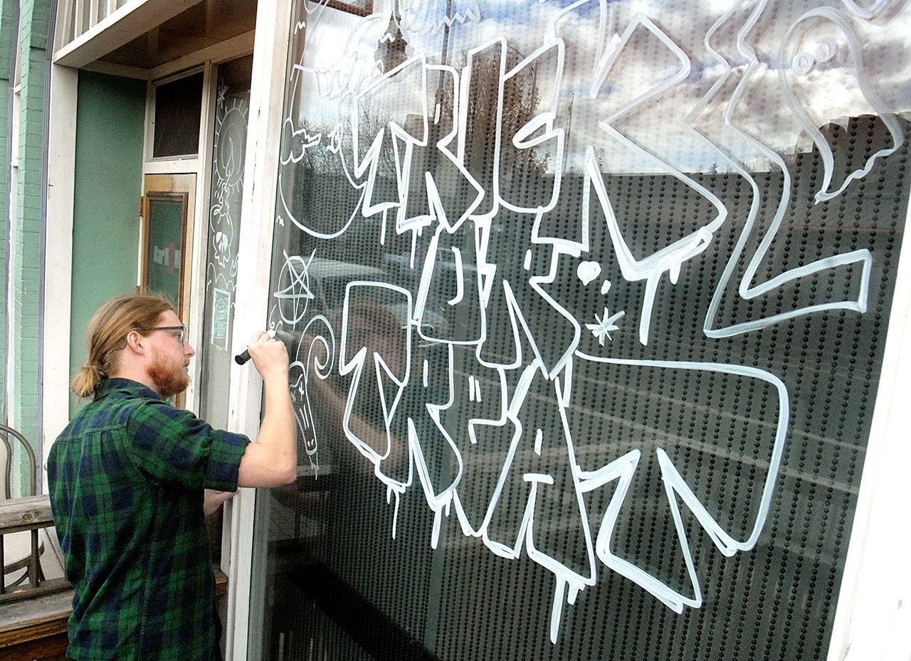 Zach Hanson, an employee of Bar N9ne restaurant and bar in downtown Port Angeles, decorates the business’ front window with a Halloween theme Friday in preparation for Monday’s holiday. (Keith Thorpe/Peninsula Daily News)