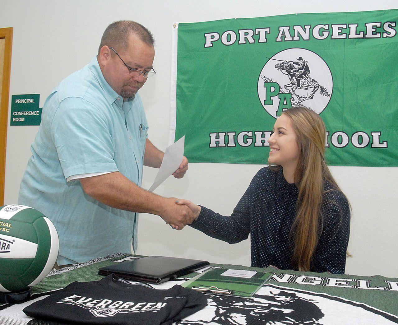 Keith Thorpe/Peninsula Daily News                                Port Angeles High School senior Kiana Robideau, seated, receives congratulations from athletic director Dwayne Johnson prior to Robideau signing a letter of intent on Wednesday to attend Evergreen State College on a volleyball scholarship.