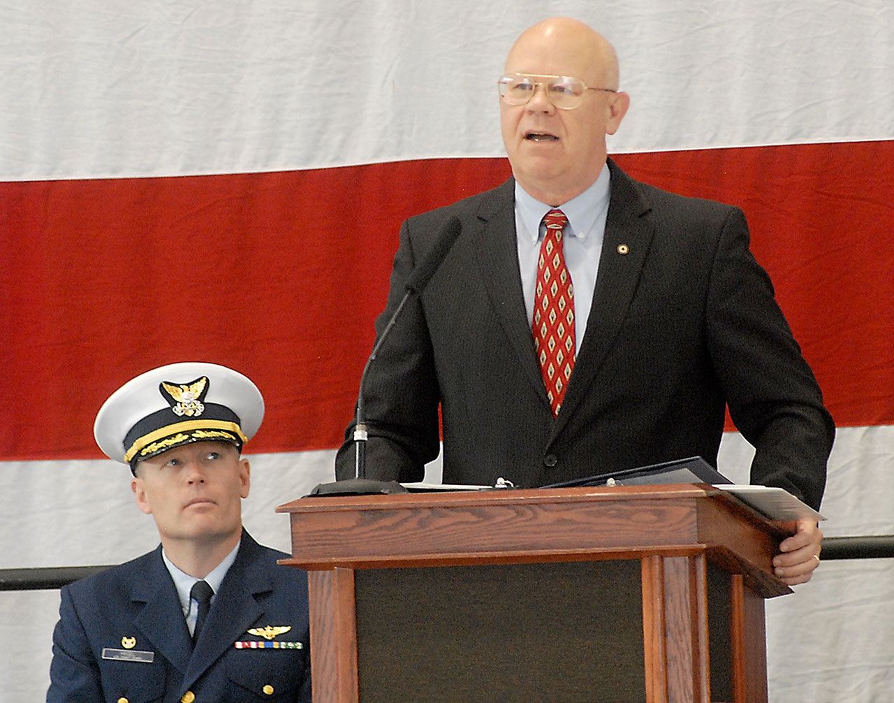 Retired U.S. Coast Guard Rear Adm. Richard Gromlich, right, delivers the keynote address during Friday’s Veterans Day ceremony in the hangar of U.S. Coast Guard Air Station/Sector Field Office Port Angeles. Looking on at left is Cmdr. Mark Hiigel, commanding officer of the station. (Keith Thorpe/Peninsula Daily News)