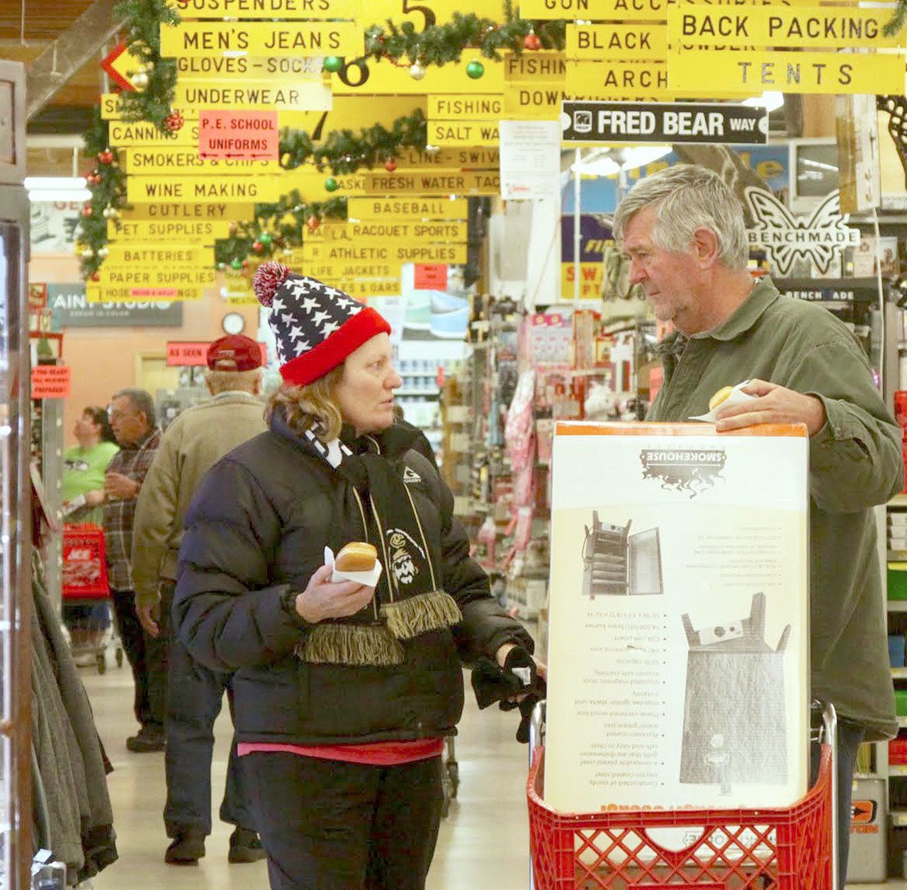 Mike and Ginny Sturgeon of Port Angeles are in the midst of shopping at 6 a.m. at Swain’s General Store early Black Friday. They came to catch a big deal on smokers (in their cart) and eat a free doughnut provided by the store for hardy early morning shoppers. (Dave Logan/for Peninsula Daily News)