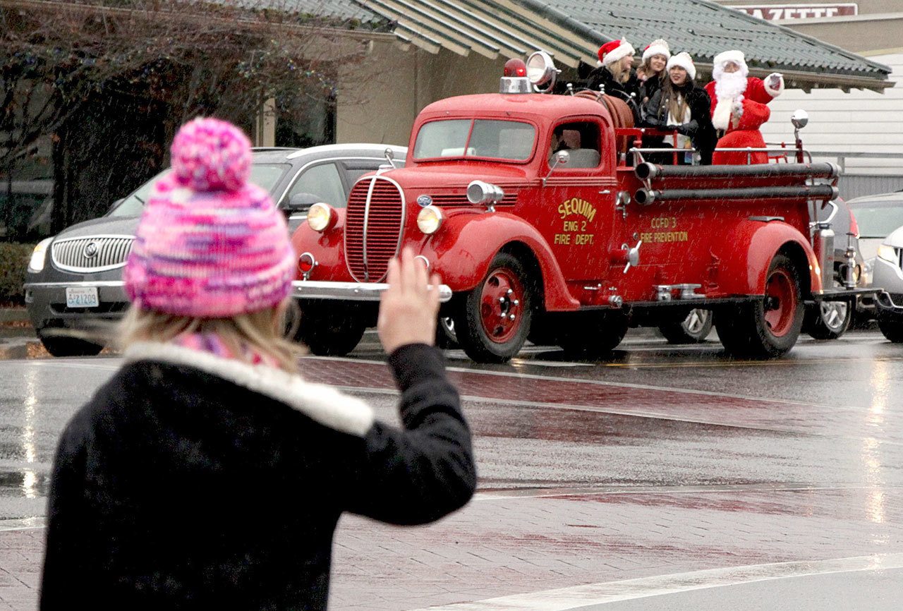 Emma Rhodes, age 6 of Sequim, stands on the corner of Sequim Ave and Washington St as Santa arrives in an old vintage Sequim fire engine on Saturday. Santa and the Irrigation Festival Court greeted all the people from the engine before they arrived at the Sequim plaza to greet children individually. (Dave Logan/for Peninsula Daily News)
