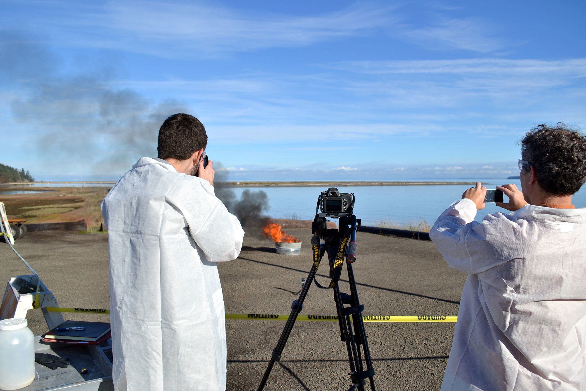 Staff with the Pacific Northwest National Laboratory watch an oil slick burn during a demonstration of how an aggregator wood product helps burn oil more efficiently in cold conditions. (Matthew Nash/Olympic Peninsula News Group)