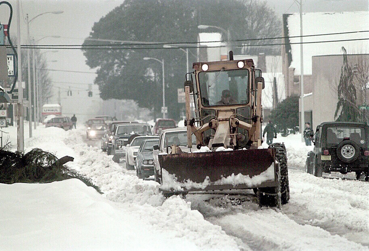 A road grader-turned-snow plow leads a procession of cars down a snow-covered section of Eighth Street in Port Angeles on Dec. 29, 1996. (Keith Thorpe/Peninsula Daily News)