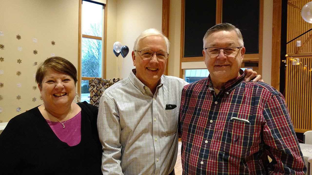 Stan Peterson stands flanked by long-time friends Carol and Larry Simmons at Peterson’s retirement party Saturday at the Forks Rainforest Arts Center. (Zorina Barker/for Peninsula Daily News)