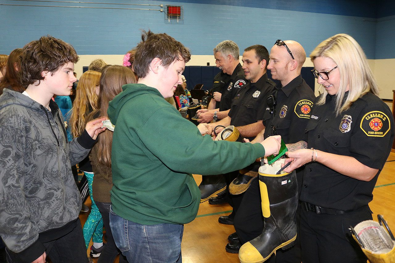 Stevens Middle School students, from left, Adam Boyd and Liam Getzin, add their dollars to local firefighters’ boots at Thursday’s assembly. Firefighters, from left, are Tim Davis, Andy Pittman, Nate Thompson and Margie Brueckner. (Port Angeles School District)