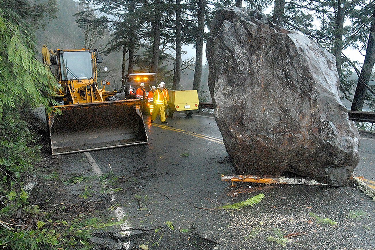 Keith Thorpe/Peninsula Daily News A Washington Department of Transportation crew looks at a giant boulder that landed on U.S. Highway 101 near milepost 228 east of Barnes Point at Lake Crescent on Thursday.