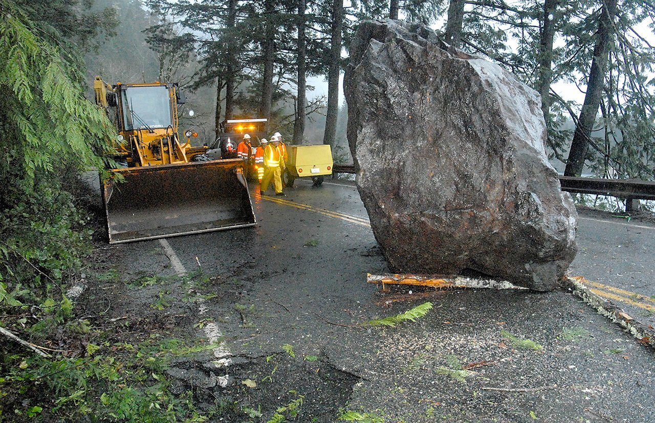 A Washington Department of Transportation crew looks at a giant boulder that landed on U.S. Highway 101 near milepost 228 east of Barnes Point at Lake Crescent on Thursday. (Keith Thorpe/Peninsula Daily News)