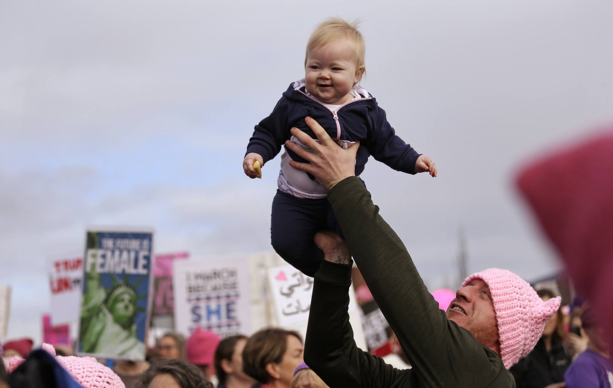 A man lifts a baby above the crowd before a women’s march Saturday in Seattle. (Elaine Thompson/The Associated Press)