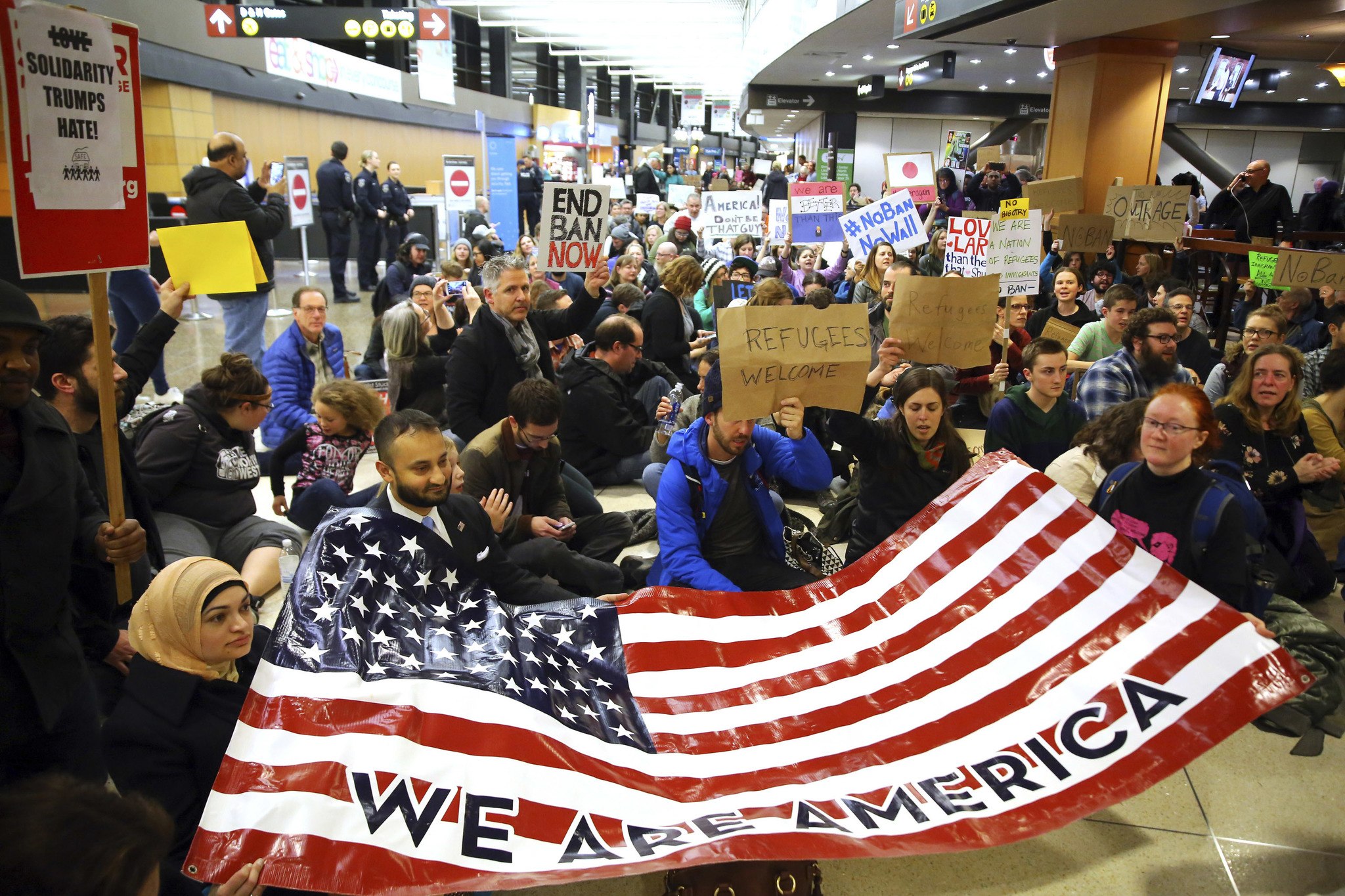 Demonstrators sit down in the concourse and hold a sign that reads “We are America” as more than 1,000 people gather at Seattle-Tacoma International Airport on Saturday to protest President Donald Trump’s order that restricts immigration to the U.S. (Genna Martin/seattlepi.com via AP)