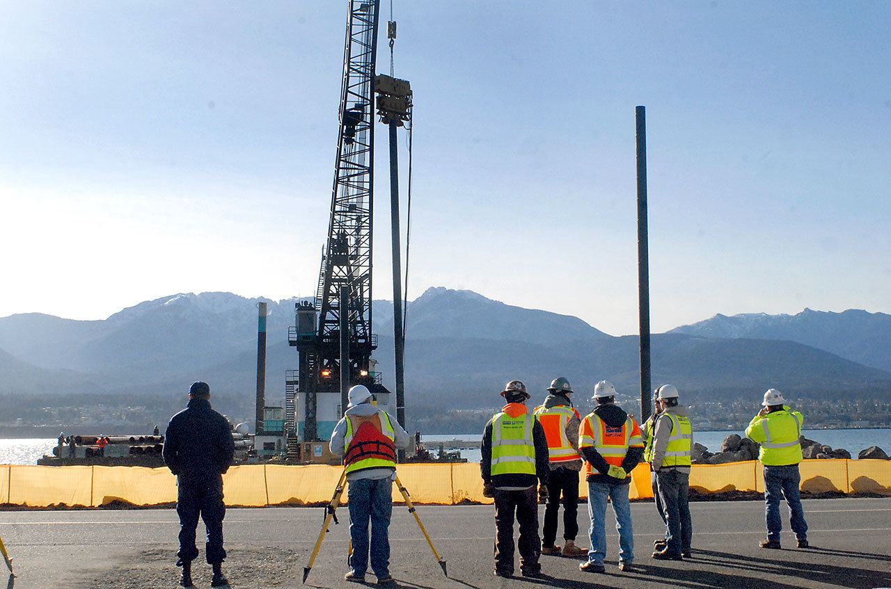Crews watch Wednesday as a floating construction crane drives the first group of pilings for what will become a new U.S. Navy escort vessel pier at U.S. Coast Guard Air Station/Sector Field Office Port Angeles on Ediz Hook. (Keith Thorpe/Peninsula Daily News)