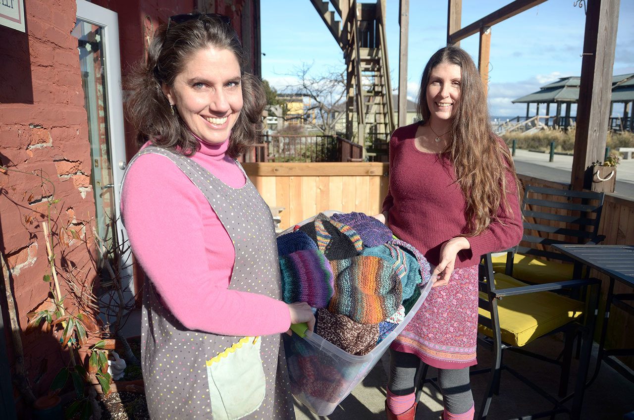 Bazaar Girls yarn shop owners Kerri Hartman and Numahka Swan hold a bucket of hats knitted for local organizations that help the homeless population in Port Townsend. (Cydney McFarland/Peninsula Daily News)