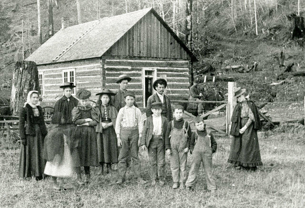 A group of unidentified adults and children stand in front of a log building in the Brinnon area in the 1890s. (Jefferson County Historial Society)