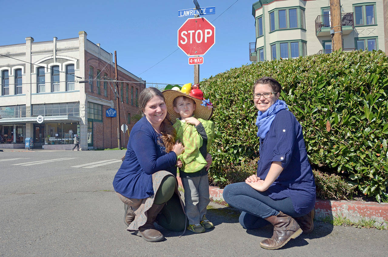 Jefferson County Farmers Market assistant manager Amy Costa Goetz and her son, Mikah, at left, wearing a farmers market hat; and market director Amanda Milholland stand on the corner of Lawrence and Tyler streets in Port Townsend, where the farmers market will kick off its 2017 season Saturday. (Cydney McFarland/Peninsula Daily News)