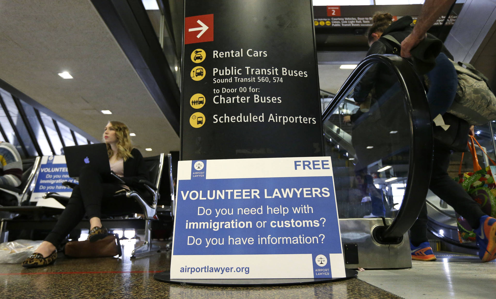 Ted S. Warren (2)/The Associated Press Asti Gallina, left, a volunteer law student from the University of Washington, sits at a station near where passengers arrive on international flights at Seattle-Tacoma International Airport on Tuesday. Gallina was volunteering with the group Airport Lawyer, which also offers a secure website and mobile phone app that alerts volunteer lawyers to ensure travelers make it through customs without trouble.