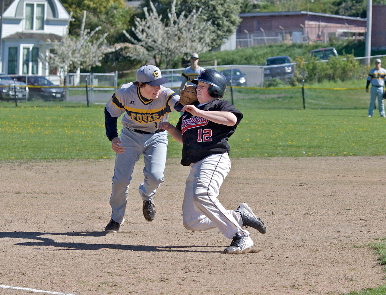 Steve Mullensky/for Peninsula Daily News                                Port Townsend’s Travis McComaghy takes it on the chin as he’s tagged out by Forks’ third baseman, Billy Palmer, during a game in Port Townsend on Monday.