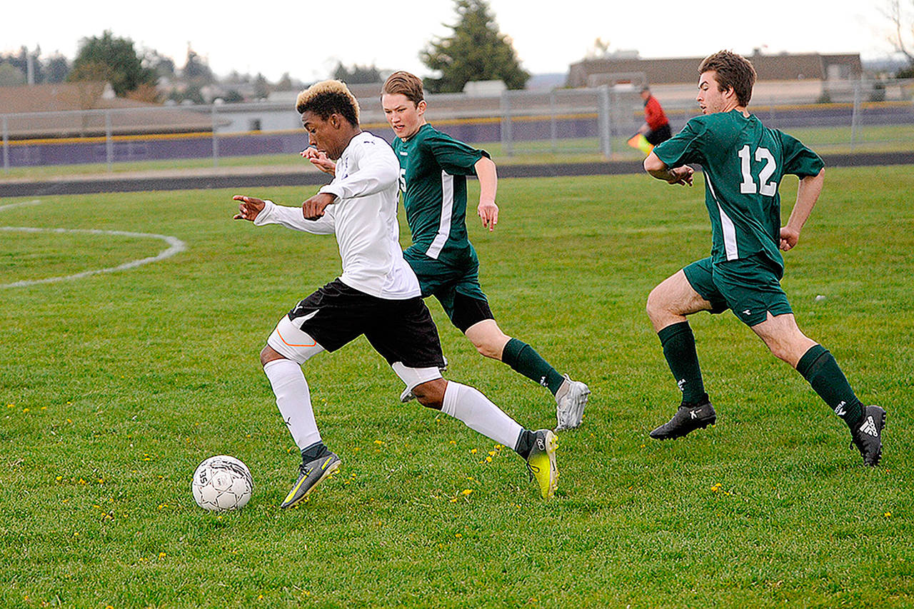 Matthew Nash/Olympic Peninsula News Group Sequim’s Josiah Urquiah, left, dribbles past Port Angeles’ Hollund Bailey (5), and Andrew Borde during the Wolves’ 5-2 win over the rival Roughriders.