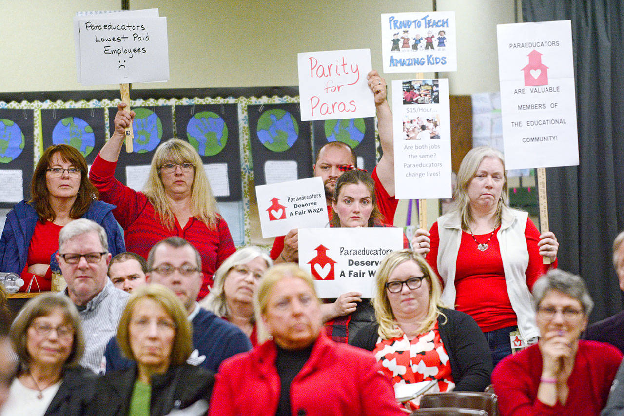People hold signs during the Port Angeles School District’s April 27 school board meeting, showing support for paraeducators as they negotiate a contract with the district. (Jesse Major/Peninsula Daily News)