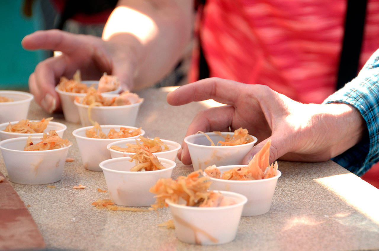 Patrons of Saturday’s farmers market dig into samples of seared salmon with spicy cabbage, prepared by Arran Stark as one of three chef demonstrations at this weekend’s Artisan Food Festival. (Cydney McFarland/Peninsula Daily News)