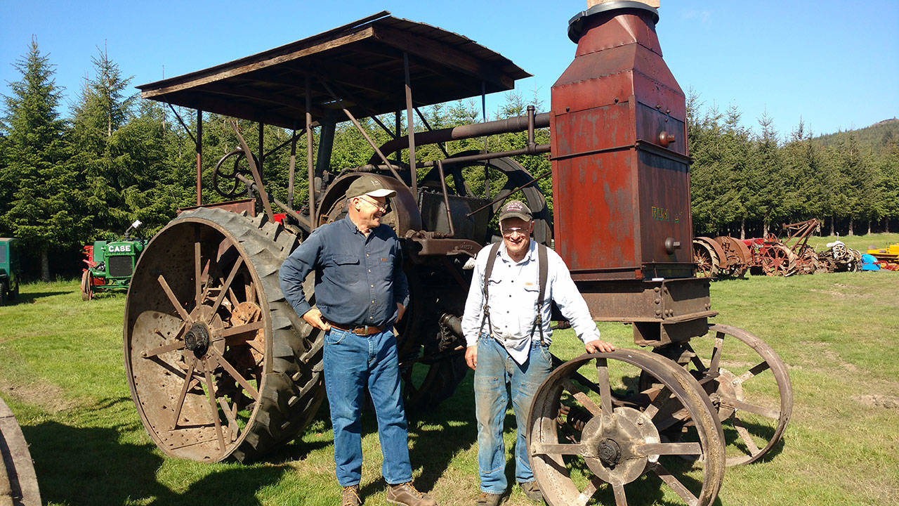 John Spoelstra and Rene Davis share a laugh in the sun near one of three classic Rumely farm tractors owned by Spoelstra’s uncle, Ted Spoelstra. (Zorina Barker/for Peninsula Daily News)