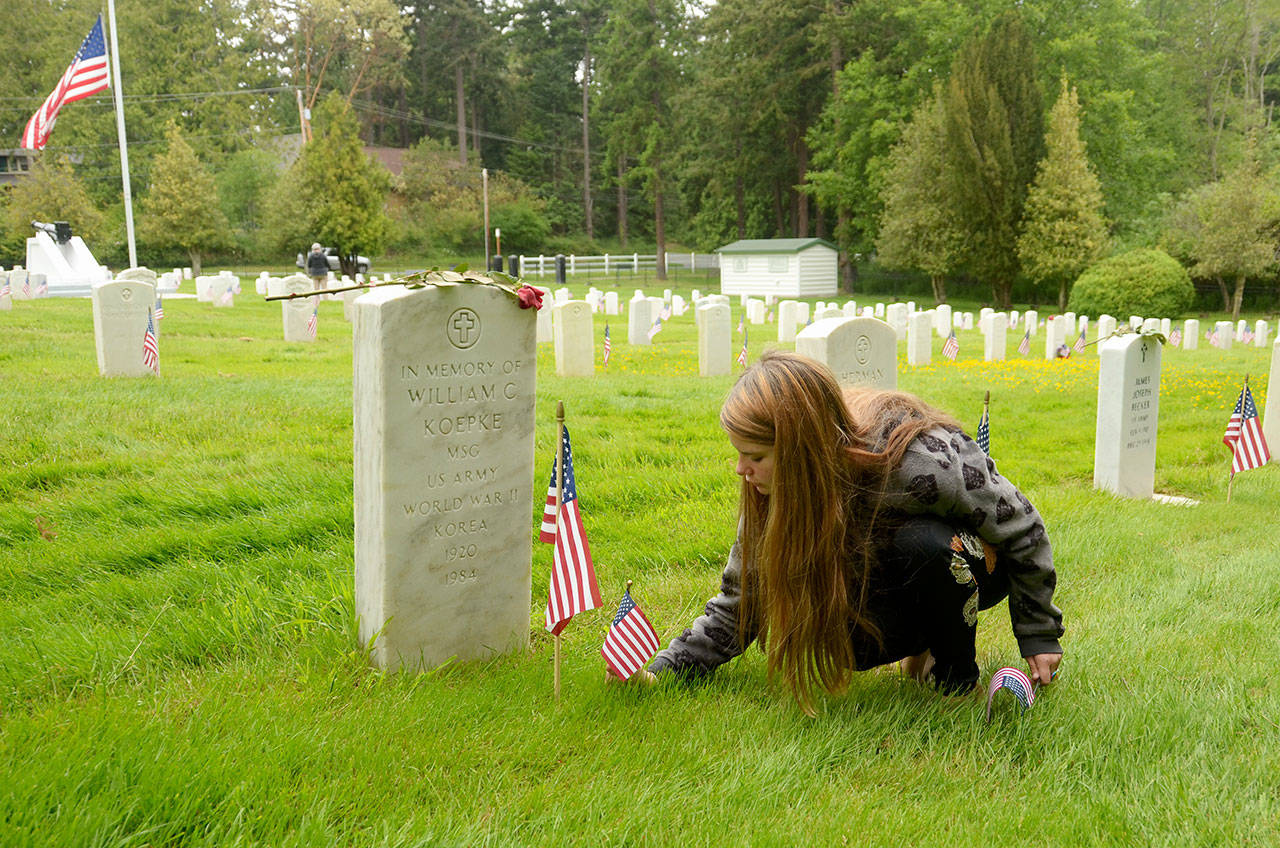 Oracle Holms of Port Hadlock places flags at the gravestones of veterans in the cemetery at Fort Worden on Monday. (Cydney McFarland/Peninsula Daily News)