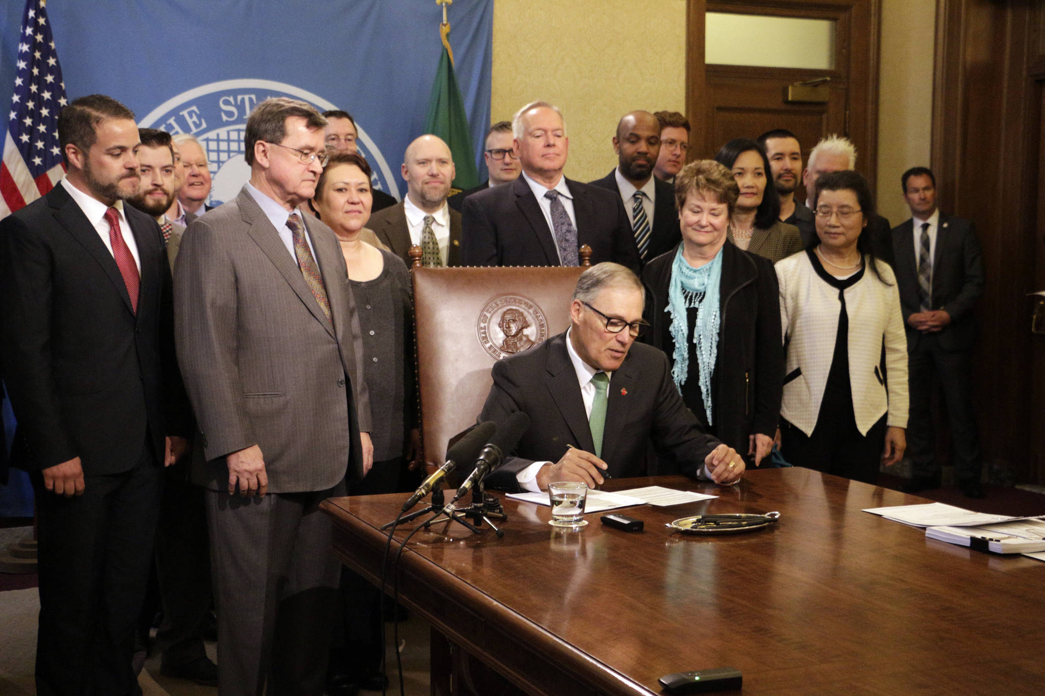 Gov. Jay Inslee, seated, prepares to sign a bill Tuesday in Olympia that seeks to bring Washington state into compliance with the federal REAL ID Act. (Rachel La Corte/The Associated Press)
