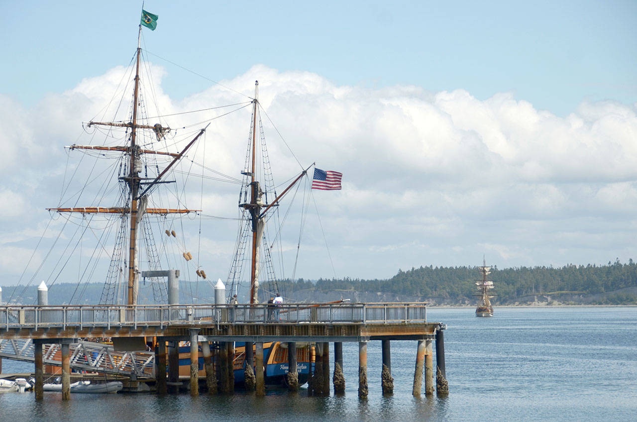 A passerby checks out the Hawaiian Chieftain, a tall ship docked at the Northwest Maritime Center, while another tall ship lowers its sails in the background, heading toward Marrowstone Island. (Cydney McFarland/Peninsula Daily News)