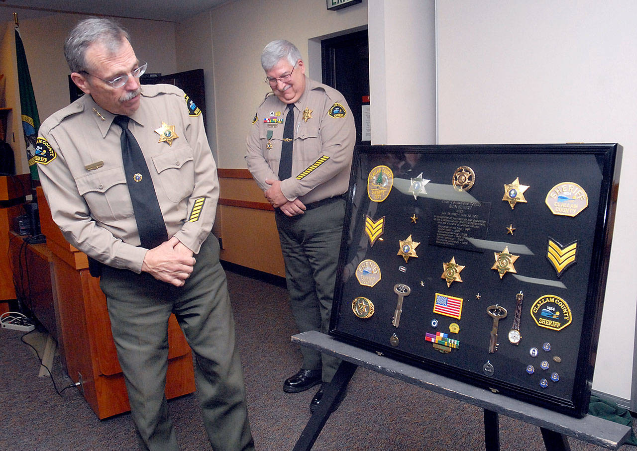 Clallam County Sheriff Bill Benedict, left, looks over a shadowbox of badges, patches and other memoribilia from the career of retiring county Jail Superintendent Ron Sukert, center, during a presentation honoring Sukert on Tuesday at the Clallam County Courthouse. (Keith Thorpe/Peninsula Daily News)