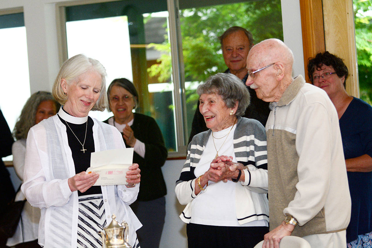 The Rev. Gail Wheatley of St. Andrews Episcopal Church, left, reads a letter from Gov. Jay Inslee congratulating Elaine and Ed Berrington, center and right, on their 75th anniversary. (Jesse Major/ Peninsula Daily News)