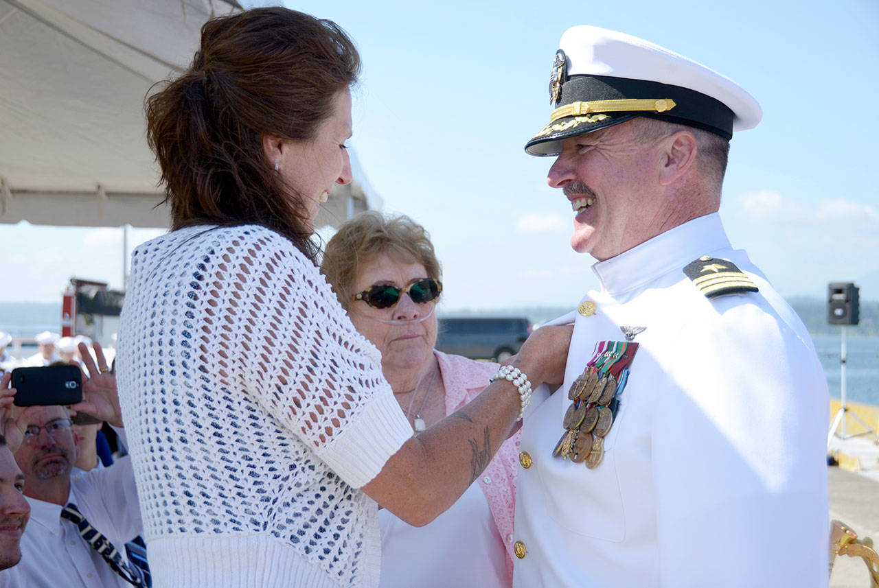 Rocky Pulley, the new commanding officer for Naval Magazine Indian Island, gets a pin placed on him by his wife, Bobbie Pulley, and mother, Cheri Pulley, during the change-of-command ceremony Thursday. (Cydney McFarland/Peninsula Daily News) ​