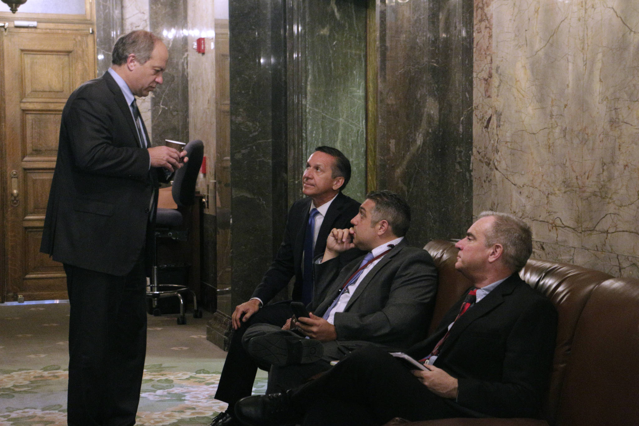 Republican state Sen. Steve O&rsquo;Ban, standing, talks with fellow Republican Sen. Dino Rossi, seated far left, and caucus staffers in the Senate wings before heading into a meeting to hear details on a state budget deal on Thursday in Olympia. A new two-year budget must be signed into law by midnight Friday in order to avoid a partial state government shutdown. (Rachel La Corte/The Associated Press)