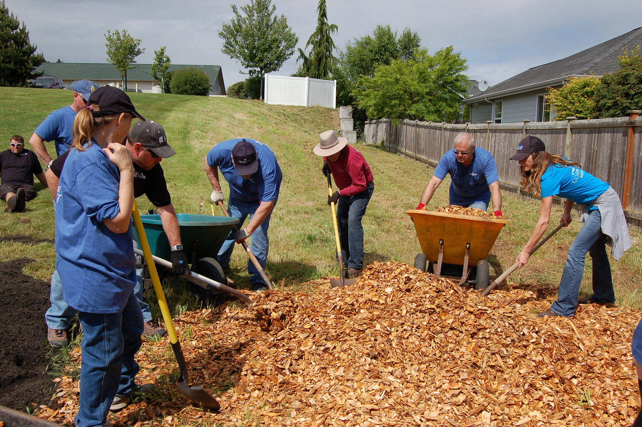 A group of Windermere brokers, All in One and Cascade Bark volunteers raked and shoveled wood chips into wheelbarrows before they poured them in the new community garden rebuilt at Sunbelt Apartments. (Erin Hawkins/Olympic Peninsula News Group)