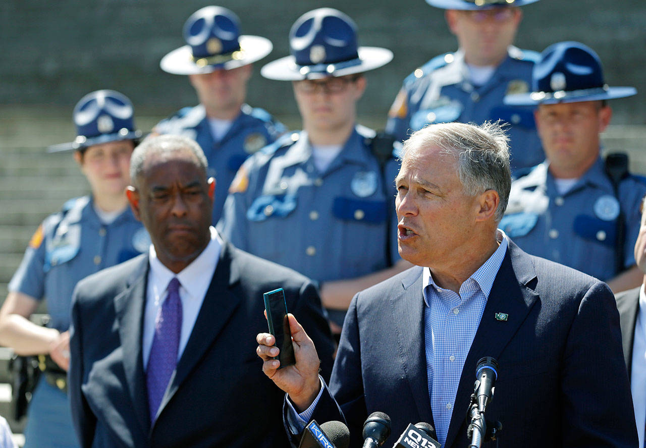 Gov. Jay Inslee, right, holds a cellphone as he speaks during a press event Monday at the Capitol in Olympia to raise awareness of the state’s new law prohibiting the use of nearly all phones and mobile devices while driving. Looking on at left is John Batiste, chief of the Washington State Patrol. The new law takes effect today. (Ted S. Warren/The Associated Press)