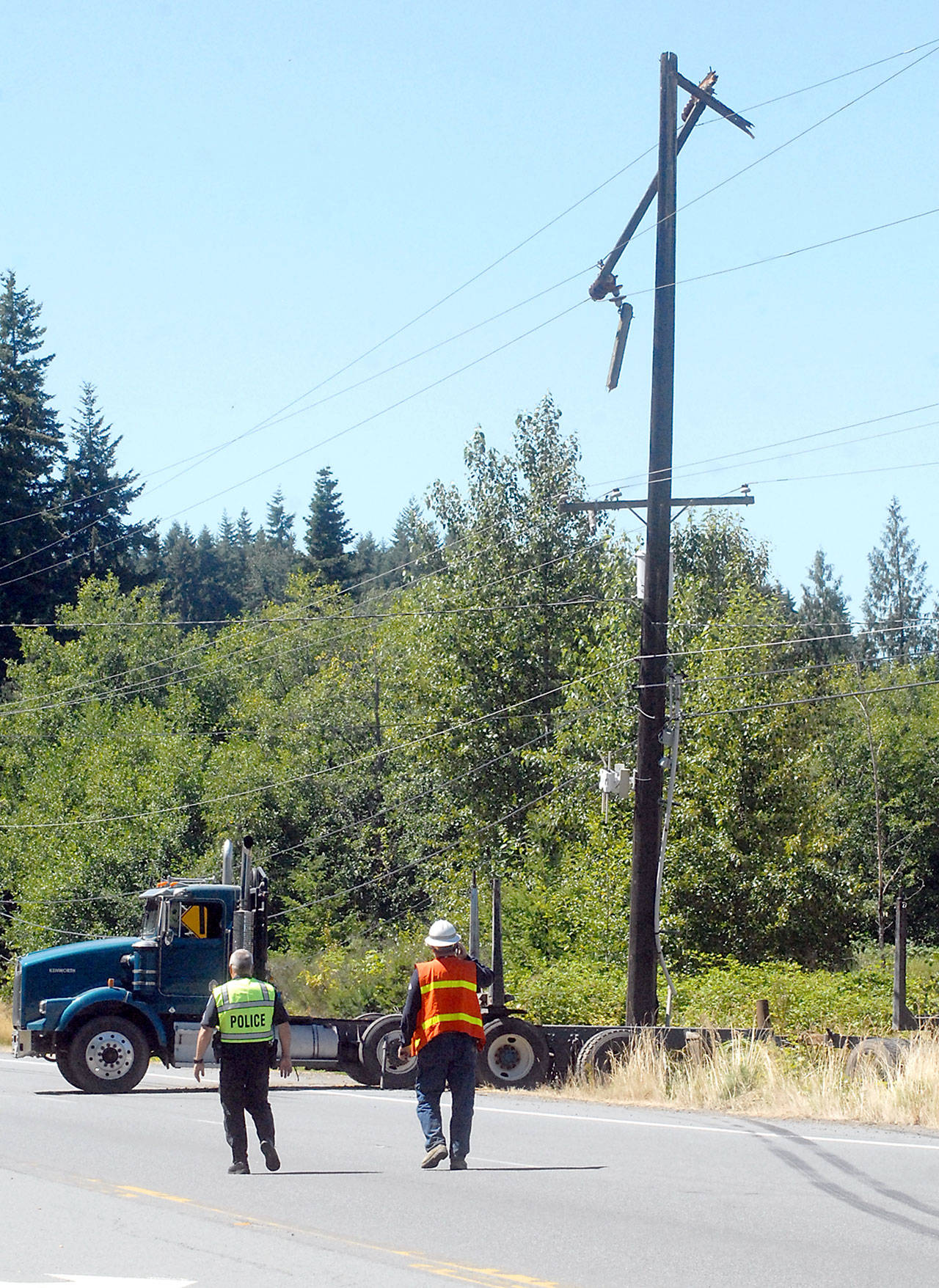 Port Angeles police and Clallam County Public Utility District 1 representatives approach an unloaded log truck that slid into a utility pole, forcing the closure of U.S. Highway 101 between Airport Road and Bean Road in Port Angeles on Tuesday. Traffic was detoured onto Edgewood Drive for the duration of the incident. (Keith Thorpe/Peninsula Daily News)