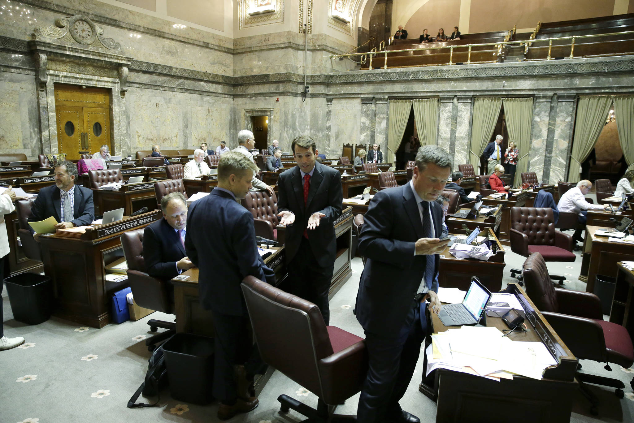 Sen. Mark Mullet, D-Issaquah, takes a phone call at right Friday after talking with Sen. Andy Billig, D-Spokane, center, and Sen. Jamie Pedersen, D-Seattle, center-left, on the floor of the Senate at the Capitol in Olympia. (Ted S. Warren/The Associated Press)
