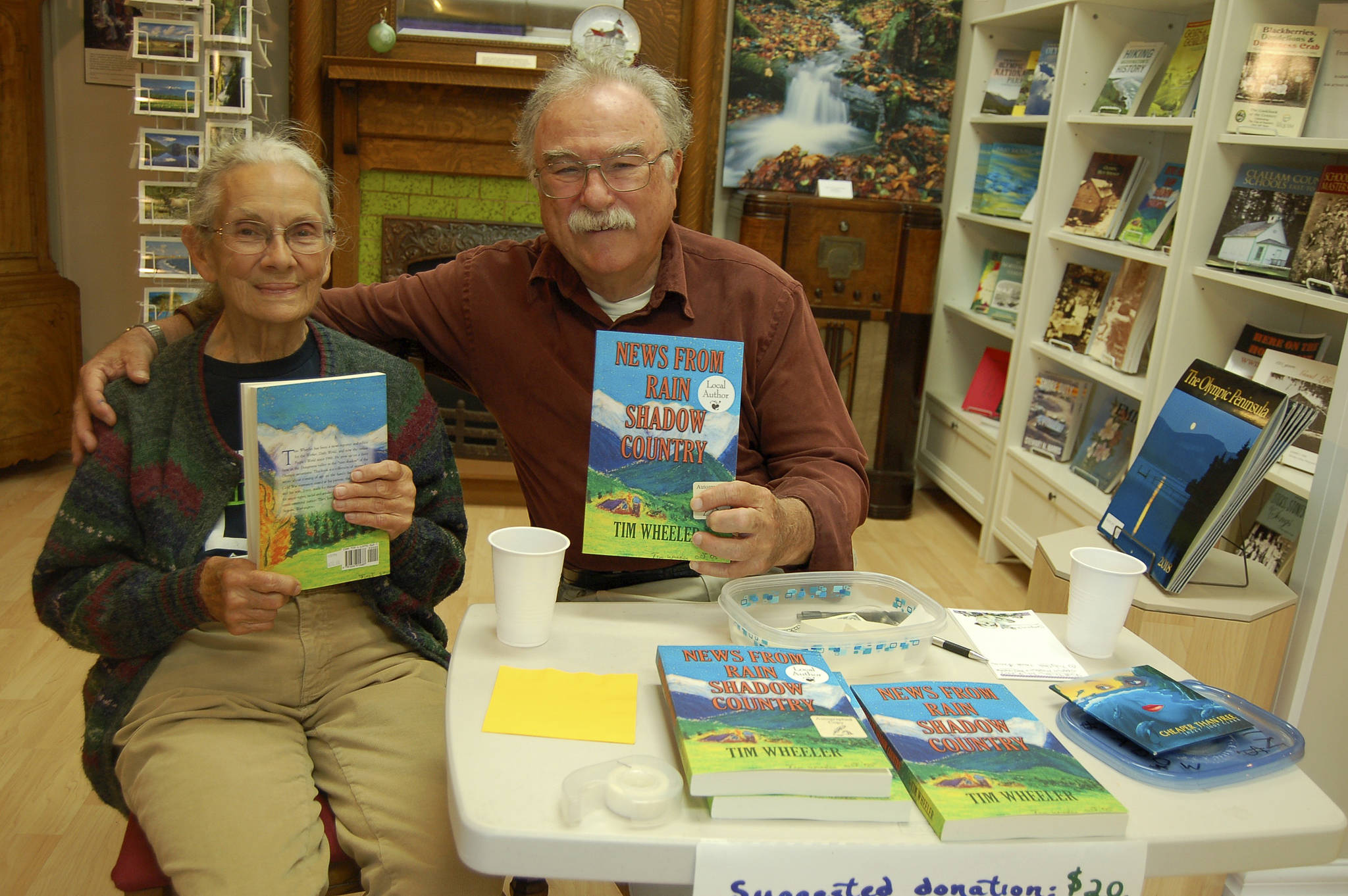 Tim Wheeler, pictured with his wife, Joyce, signs copies of “News from Rain Shadow Country” at Sequim Museum & Arts in early July. (Erin Hawkins/Olympic Peninsula News Group)