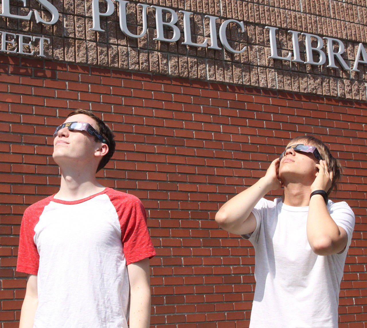 Port Angeles residents Jesse Driese, 14, and James Saskowsky, 13, try out eclipse glasses at the Port Angeles Library. On Monday, the library will hand out about 50 glasses for its solar eclipse event on a first-come, first-served basis. (David Logan/for Peninsula Daily News)