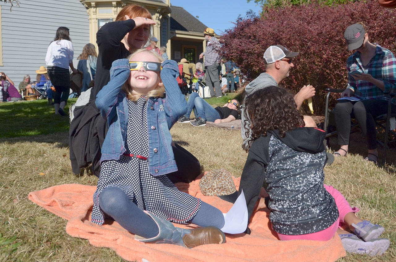 Fallon Brewer uses a pair of protective glasses handed out by the Friends of Port Townsend Library to watch Monday’s eclipse with Evette Brewer and Demetria Brewer. (Cydney McFarland/Peninsula Daily News)