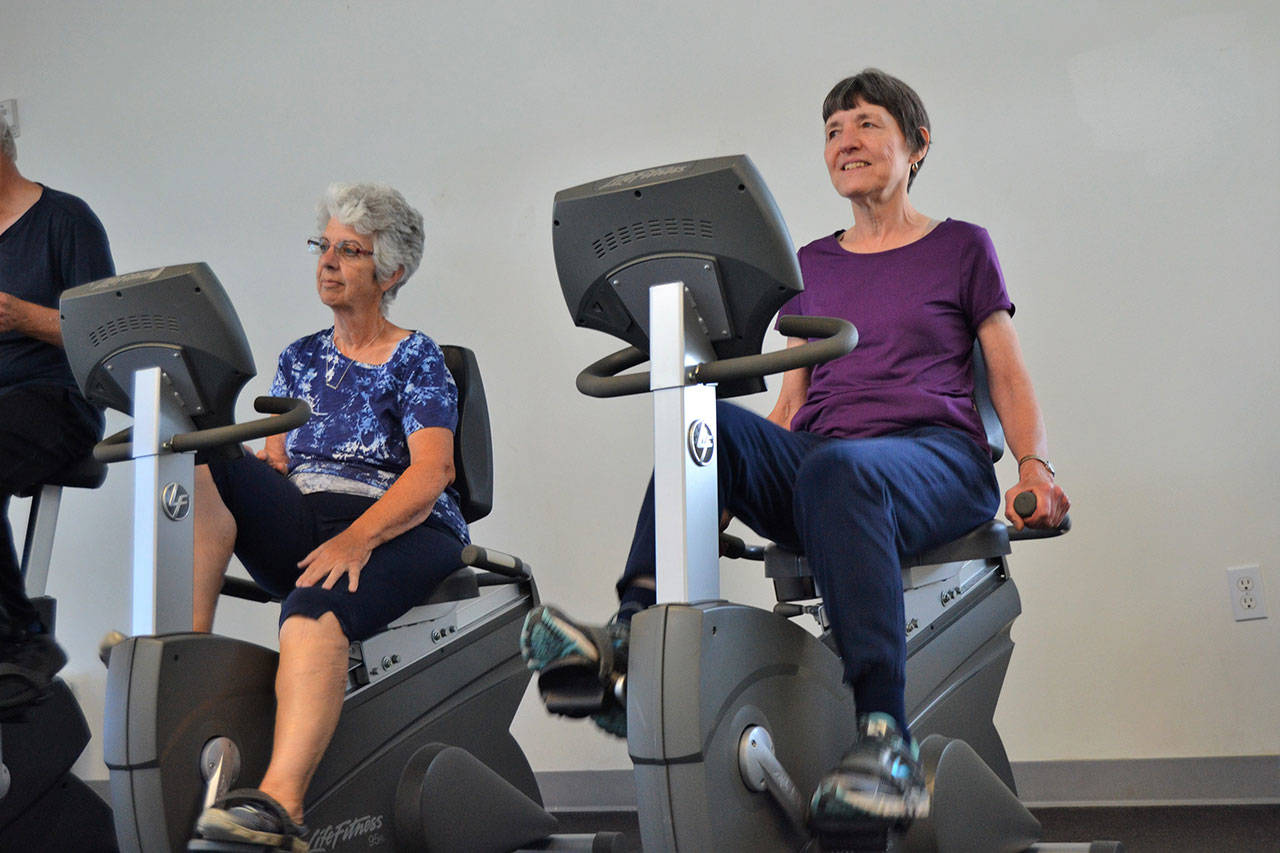 Linda Flores of Port Angeles, left, and Mary Farley of Sequim cycle at the YMCA of Sequim on Monday during a workout with the Exercise and Thrive program. (Matthew Nash/Olympic Peninsula News Group)