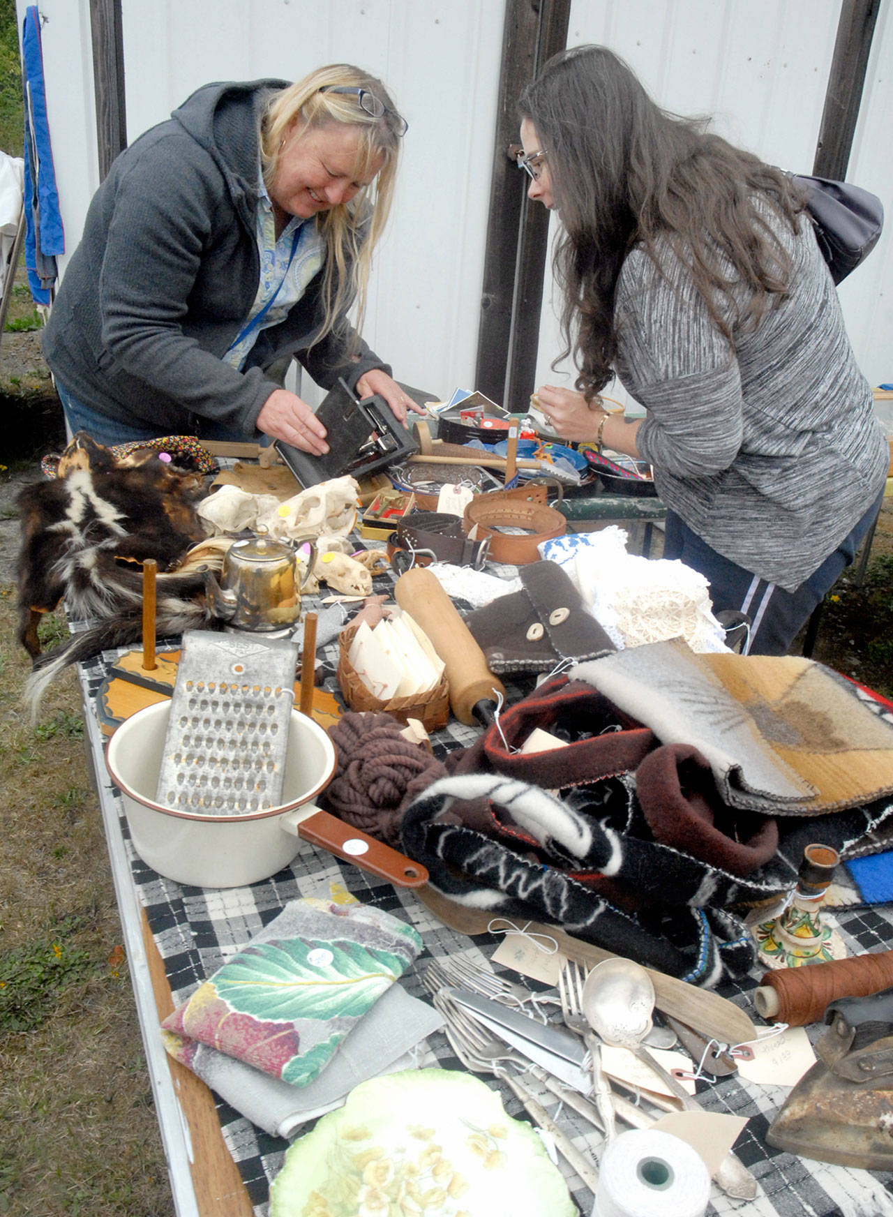 Vendor Lisa Young of Joyce, left, and Colleen Bradley of Sequim look at an antique camera at Young’s table near the Joyce Museum in Joyce as part of last year’s Great Strait Yard Sale. (Keith Thorpe/Peninsula Daily News)