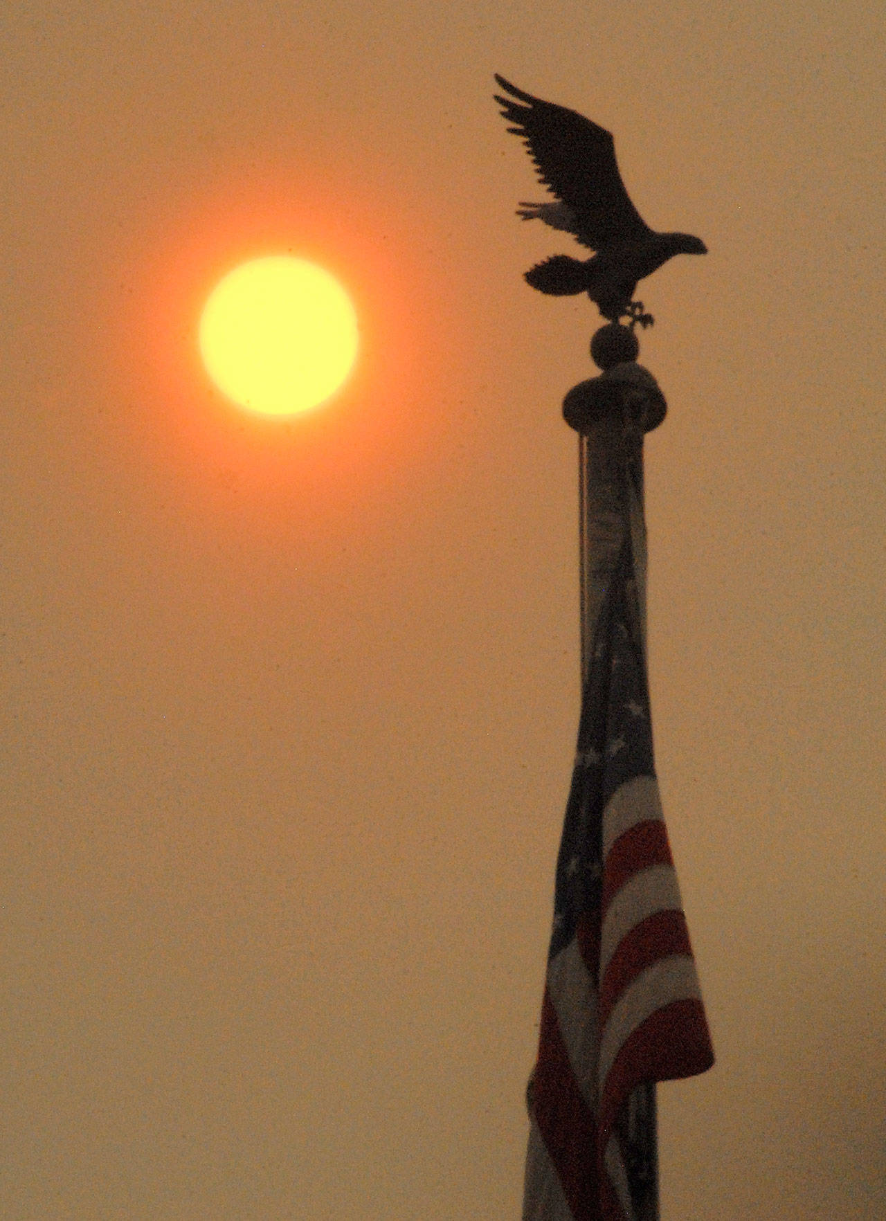 The sun shines behind a flagpole in front of the Clallam County Courthouse in Port Angeles at midmorning Tuesday as layers of smoke from wildfires in Eastern Washington and Montana filter the light to shades of orange and red. (Keith Thorpe/Peninsula Daily News)