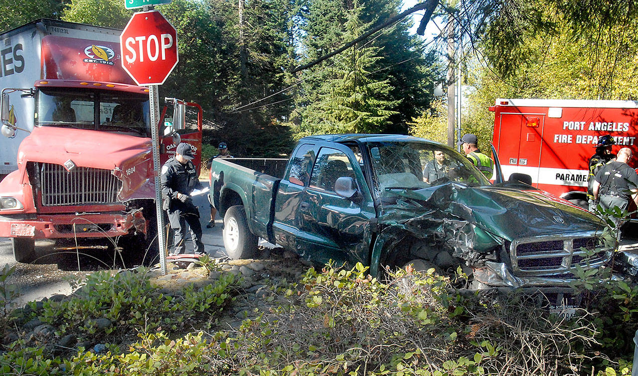 Port Angeles police Officer T.J. Mueller, left, investigates the scene where a pickup truck and a semitruck collided at the intersection of 10th and N streets in Port Angeles on Tuesday. (Keith Thorpe/Peninsula Daily News)