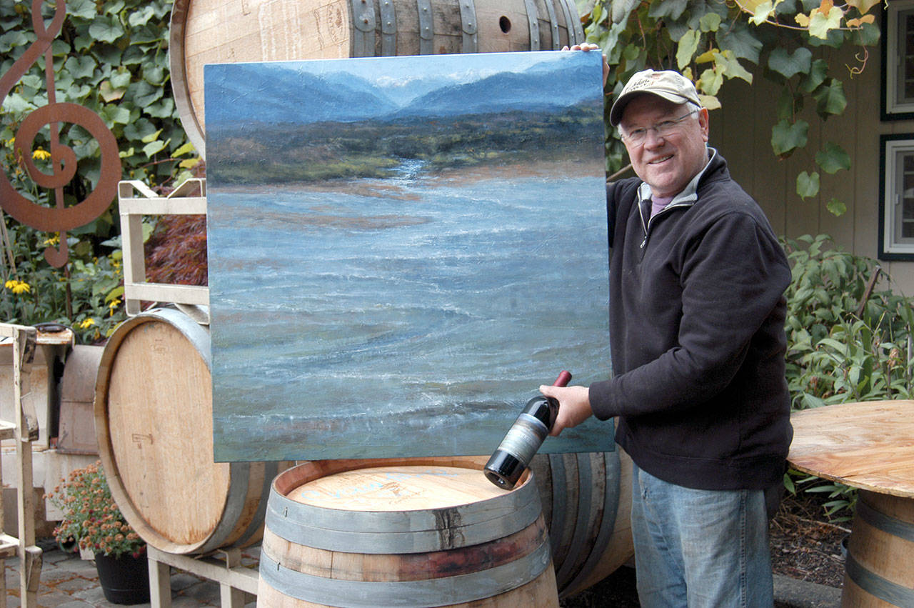 Camaraderie Cellars winemaker and co-owner Don Corson poses with Sandy Byers’ painting featured on “Confluence,” a bottle of wine that benefits the Olympic Medical Center Foundation. (Sarah Sharp/Peninsula Daily News)