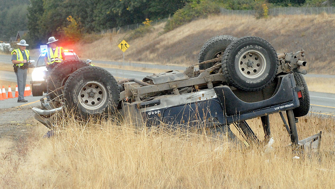 Washington State Patrol Troopers Matthew Phillips, left, and Eric Ellefson investigate the scene where a Jeep rolled over on the side of the U.S. Highway 101 exit ramp to River Road in Sequim on Friday. (Keith Thorpe/Peninsula Daily News)